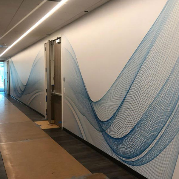 Long corridor wall covered in a printed blue wave line-art mural in a Sacramento office